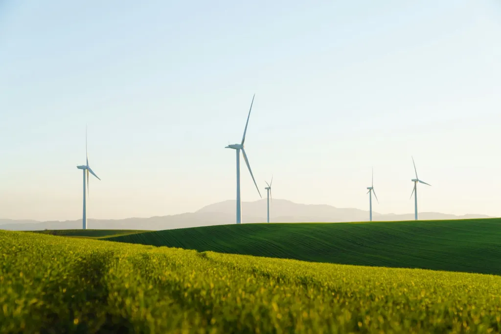 Row of white wind turbines standing behind a green grass field
