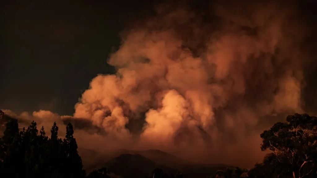 Large plume of wildfire smoke rising above a forested hillside