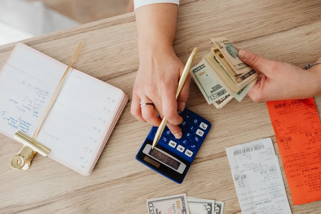 Hands holding paper bills while using a calculator on a table