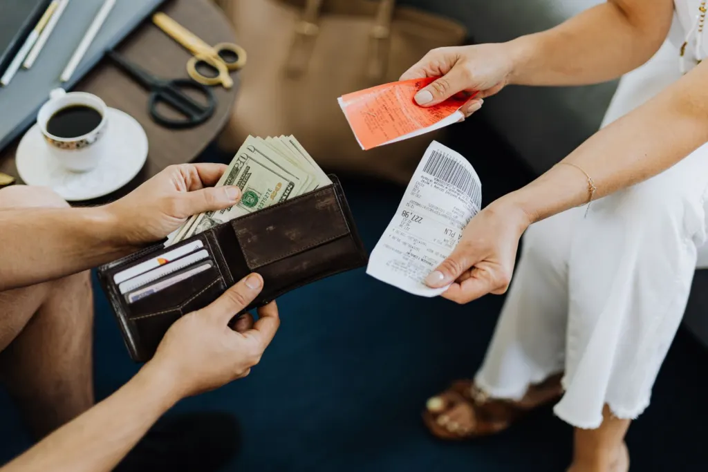 Hands pulling cash from a wallet over a wooden table