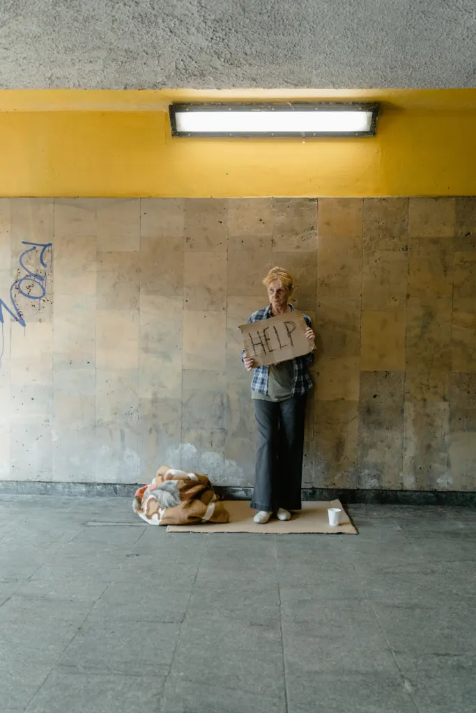 An older woman holding a handwritten cardboard sign in an underpass